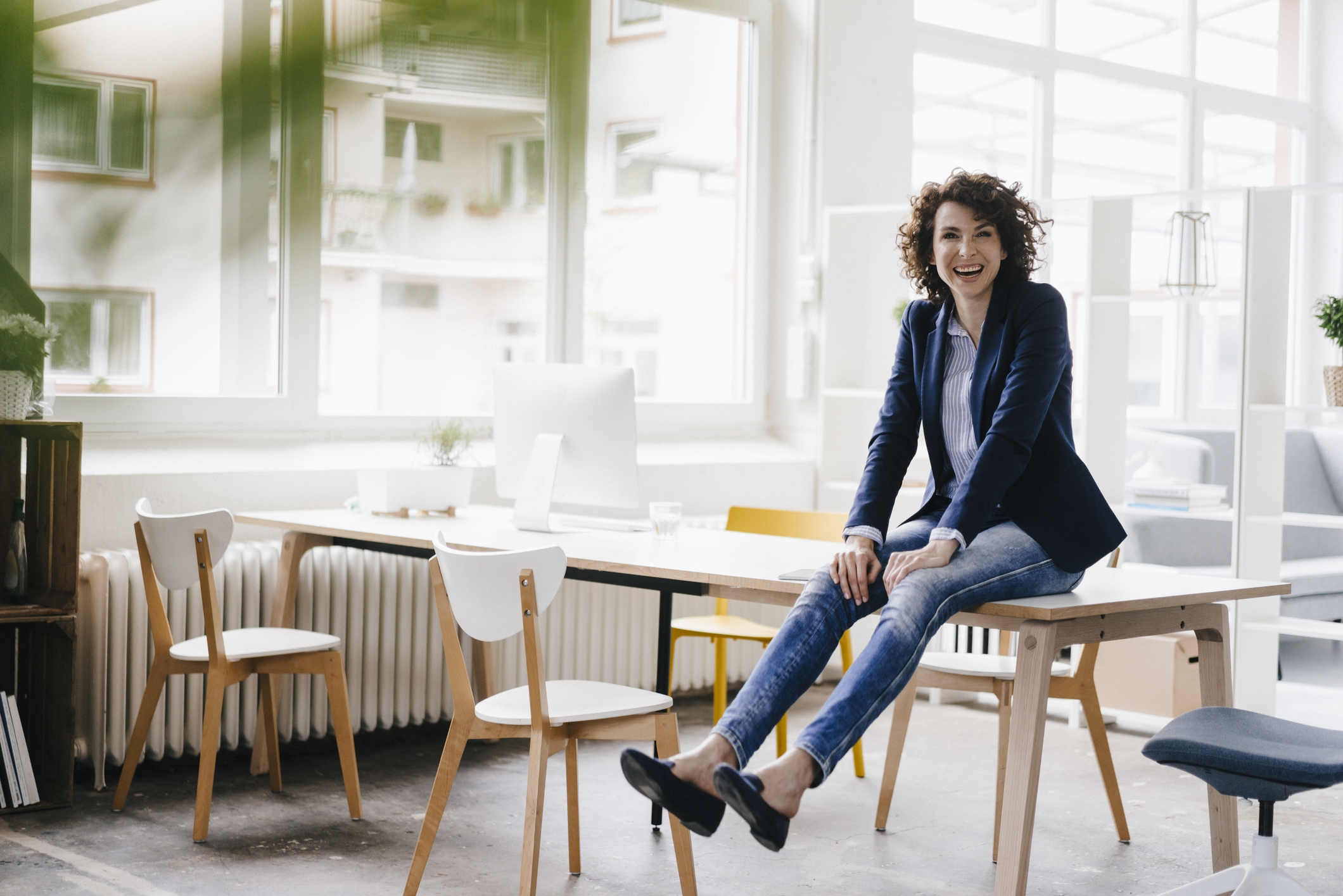 Resilienz aufbauen - Frau sitzt auf einem Bürotisch und lacht